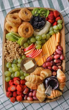 a wooden tray filled with assorted fruits and pastries on top of a checkered table cloth