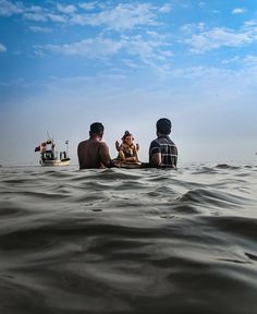 three people sitting in the water with a dog on their lap and a boat behind them