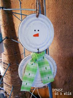 a paper plate snowman ornament hanging from a wire fence with green ribbon