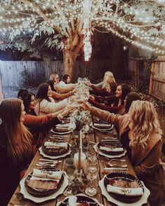 a group of women sitting around a table with plates and glasses on it, all holding hands