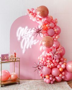 a pink balloon arch with stars and balloons on the top, next to a table