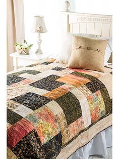 a bed with a quilt on top of it next to a night stand and lamp