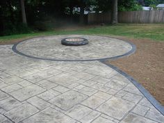 an outdoor fire pit in the middle of a brick patio with grass and bushes behind it