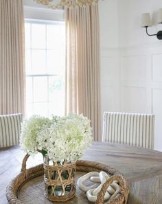 a basket with flowers on top of a table in front of a window and chairs