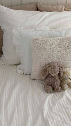 two stuffed animals sitting on top of a white bed next to pillows and pillow cases