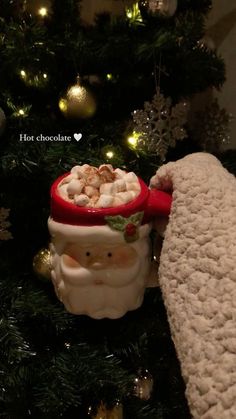 a christmas ornament with a santa clause holding a bowl of hot chocolate in front of a tree