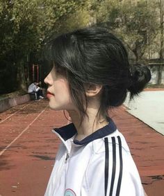 a woman standing on a tennis court with her hair in a bun and wearing a white shirt