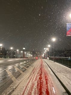 snow is falling on the road and street lights are lit up in the night sky