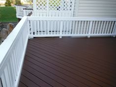 a deck with white railings and brown wood flooring in front of a house