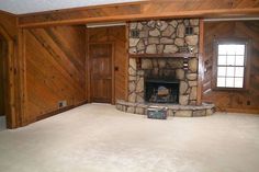 an empty living room with wood paneling and stone fireplace