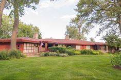 a red house sitting in the middle of a lush green field next to trees and bushes