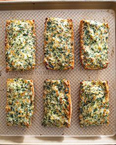 four square pieces of bread with cheese and spinach on top sitting on a baking sheet