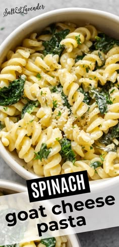 a white bowl filled with pasta and spinach on top of a table next to a spoon