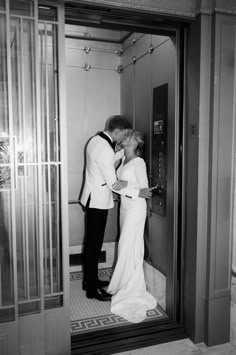 a man and woman kissing while standing in front of an open elevator door with their arms around each other