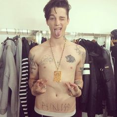 a shirtless man with his tongue out in front of some clothes and shirts on hangers