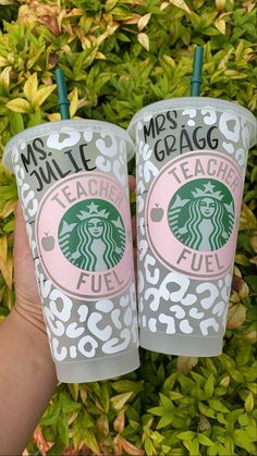 two starbucks cups are shown in front of some bushes