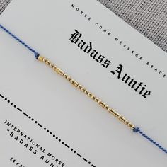 a blue string bracelet with gold beads on top of a white piece of paper next to an envelope