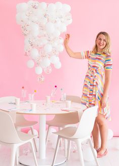 a woman standing in front of a table with white chairs and balloons hanging from the ceiling