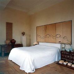 a bed sitting in a bedroom next to a wooden dresser and table with two vases on it