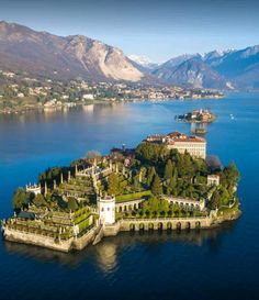 an island in the middle of water with buildings on it and mountains in the background