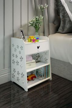 a white nightstand with flowers and books on it next to a bed in a bedroom