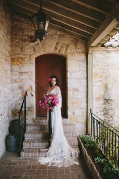 a woman in a wedding dress standing on the steps with her bouquet and looking at the camera