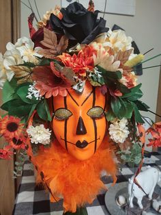 an orange mask decorated with flowers and leaves on top of a checkered table cloth