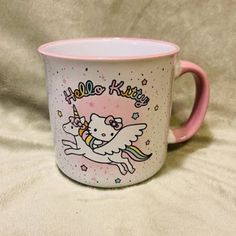 a pink and white coffee mug with an unicorn on it's side that says hello kitty