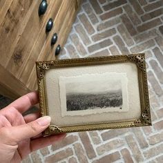 a person holding up a framed photo in front of a brick wall and flooring