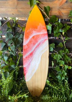 an orange and white surfboard sitting on top of green plants next to a wooden fence