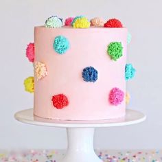 a pink cake with multicolored pom - poms on it sitting on a white pedestal