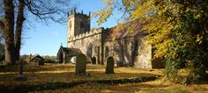 an old church surrounded by trees and grass with autumn leaves on the ground around it