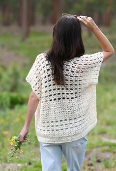 a woman walking in the woods with her back to the camera, wearing a crocheted sweater