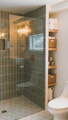 a white toilet sitting next to a shower in a bathroom with green tiles on the walls