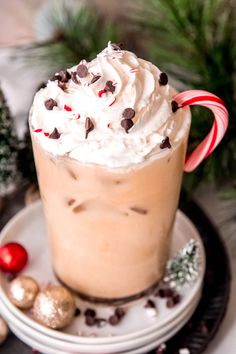 a hot chocolate drink with whipped cream and candy canes on a plate next to christmas decorations