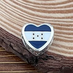 a blue and white heart shaped brooch with three stars on the center, sitting on top of a piece of wood