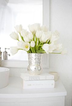 white flowers in a silver vase on top of two books next to a bathroom sink