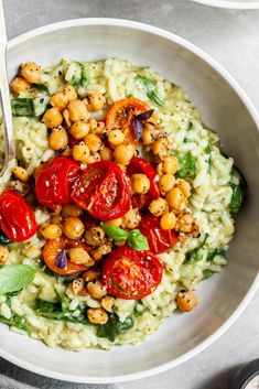 a white bowl filled with rice, tomatoes and chickpeas next to a spoon