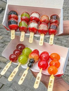 there are many different kinds of fruit on the sticks in this box, and one is being held by someone's hand