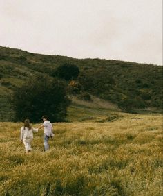 two people are walking through the grass holding hands