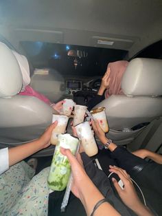 several people are sitting in the back seat of a car and drinking drinks from cups