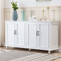 a white sideboard with three doors and two vases on top of it in a living room