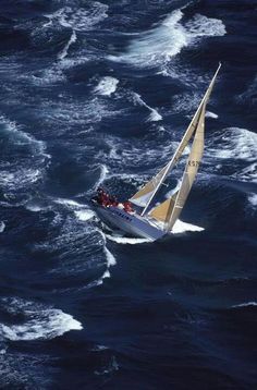 an aerial view of a sailboat in the ocean with people on it's side