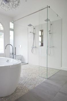 a large white bath tub sitting next to a walk in shower and a sink under a crystal chandelier