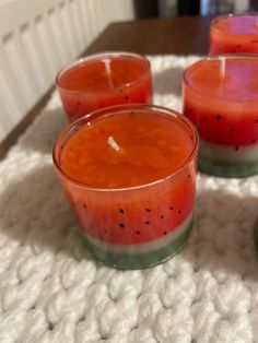 four candles sitting on top of a white blanket next to a cup filled with watermelon