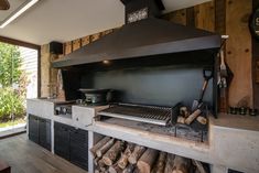 an outdoor kitchen with wood logs stacked on the counter and a large black stove top