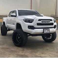 a white toyota truck parked in front of a building with black tires and rims