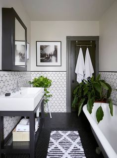 a bathroom with black and white tile, green plants, and pictures on the wall