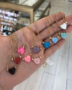 a person's hand holding five different heart necklaces in various colors and shapes