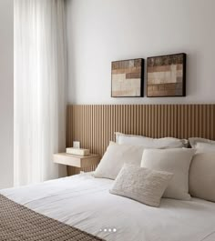 a bed with white sheets and pillows next to a wooden headboard in front of a window